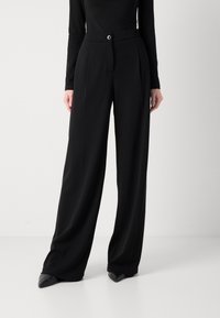 Pantaloni neri a gamba larga con fronte piatto, bottone in vita e pieghe sartoriali. Realizzati in un tessuto liscio per un aspetto elegante e moderno.