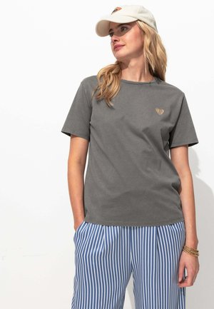 T-shirt en coton gris à manches courtes et col rond, avec un petit logo en forme de cœur doré sur la poitrine. Associé à un pantalon rayé bleu et blanc.