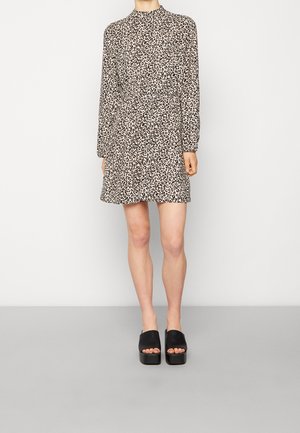 Robe à manches longues en imprimé léopard avec un col montant, taille cintrée et jupe évasée. Portée avec des sandales à plateforme noires.