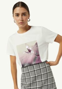 Witte katoenen t-shirt met korte mouwen, voorzien van een grote grafische print in roze en zilver. Gepaard met een zwart-wit geblokte rok.