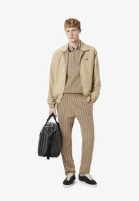 Beige bomberdzseki egy textúrált barna szett felett, geometrikus mintákkal. Fekete tornazsák pántokkal, barna sportcipők.