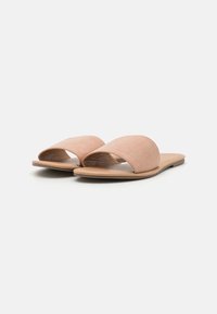 Åpne tå slip-onsandaler laget av myk, lys rosa semsket skinn med flat såle og buet design. Enkel og minimal estetikk.