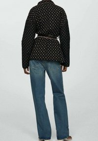 Czarna kurtka w wzory z szerokimi rękawami, z paskiem w talii i teksturowanym wykończeniem, zestawiona z jasnoniebieskimi jeansami o prostym kroju.