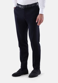 Marineblaue, maßgeschneiderte Hose mit flacher Vorderseite, aus glattem Stoff, kombiniert mit einem schwarzen Ledergürtel und dunklen Wildleder-Slippern.