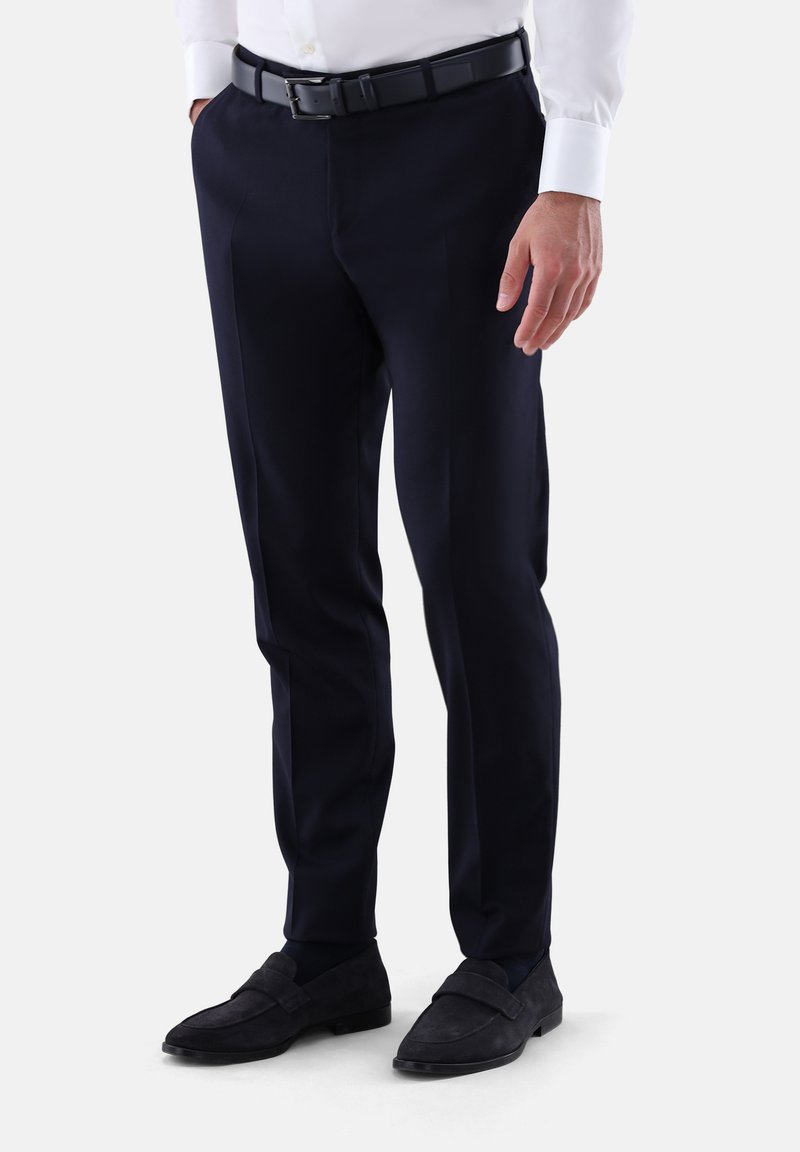 Marineblaue, maßgeschneiderte Hose mit flacher Vorderseite, aus glattem Stoff, kombiniert mit einem schwarzen Ledergürtel und dunklen Wildleder-Slippern.