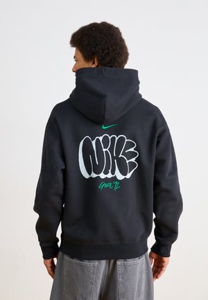 Felpa nera in cotone, con una grande stampa grafica bianca e verde sul retro che recita "Nike dal '92". Vestibilità standard con cappuccio.