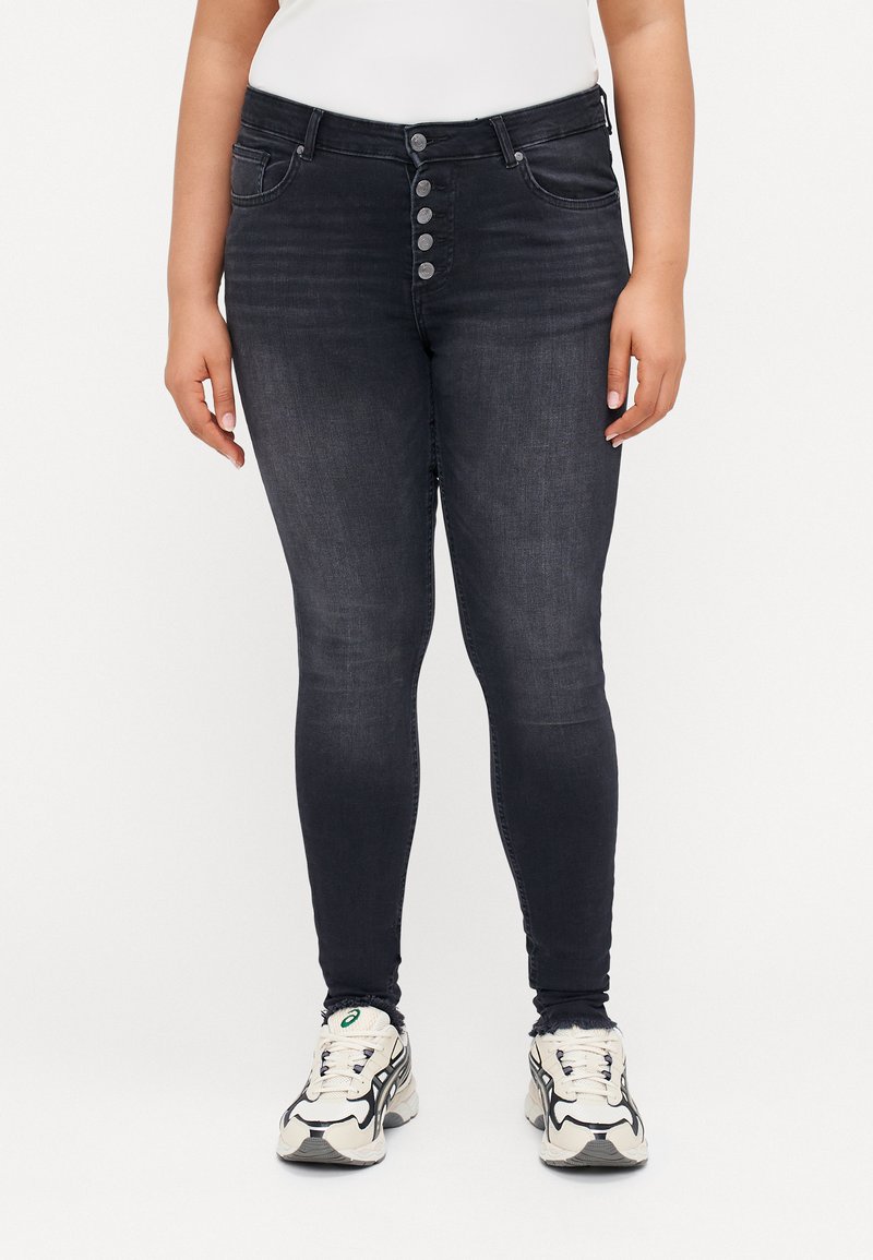 Black denim skinny jeans with a smooth texture, five-button closure, front pockets, and fitted design. Styled with white top and sneakers.