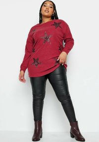 Röd ribbad tröja med svarta paljetterade stjärnor, kombinerad med svarta leggings i konstläder och burgundy ankelstövlar. Slät textur och avslappnad passform.