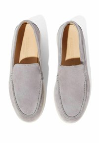 Een paar lichtgrijze suède instaploafers met gestikte details en beige zolen, van bovenaf weergegeven op een witte achtergrond.