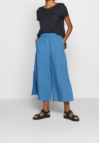 Blue linen culottes with an elastic waistband and side slits, paired with a fitted black short-sleeve top and black sandals.