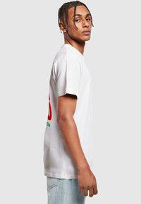 White cotton t-shirt featuring a large red graphic design with green accents. Short sleeves and a classic crew neck shape.