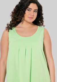 Top senza maniche verde chiaro con scollatura rotonda e design plissettato sulla parte frontale, realizzato in un tessuto morbido che drappeggia liberamente attorno al corpo.