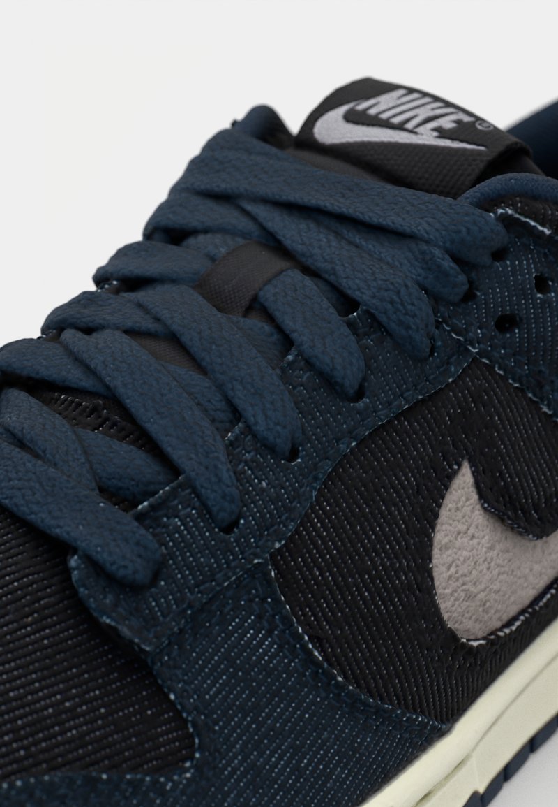 Baskets Nike avec un dessus texturé bleu marine, des accents noirs et un logo gris clair. Le design comprend des lacets épais et une languette rembourrée.