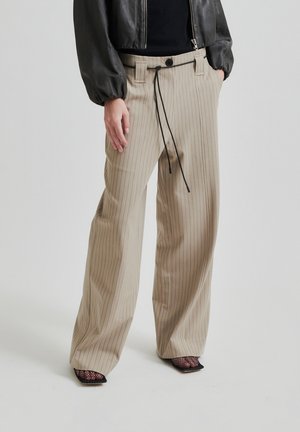 Pantaloni beige a righe con una vestibilità comoda, girovita con cordoncino e tasche. Abbinati a tacchi in rete neri e a un top aderente nero.