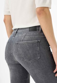 Jeans in denim grigio con un design aderente, dotati di due tasche posteriori e un'etichetta nera posizionata sulla vita. Tessuto liscio.