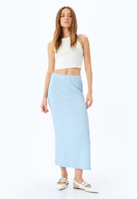 Lichtblauwe gebreide lange rok met een gestructureerde afwerking, gecombineerd met een witte cropped mouwloze top en witte hakken.