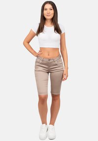 Shorts bermuda beige avec des détails de couture blanche, dotés d'une fermeture à bouton et de poches avant, associés à un T-shirt blanc court et des baskets blanches.