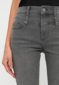 Γκρι τζιν από τζιν ύφασμα με εφαρμοστή γραμμή, μέση μεσαίου ύψους, μπροστινές τσέπες και κλείσιμο με μεταλλικό κουμπί, με λεία, υφή φινίρισμα.