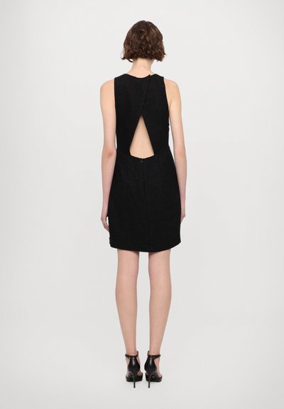 Vestido negro sin mangas con un corte en la espalda y cierre de cremallera. La tela tiene un acabado texturizado. Se lleva con tacones negros de punta abierta.