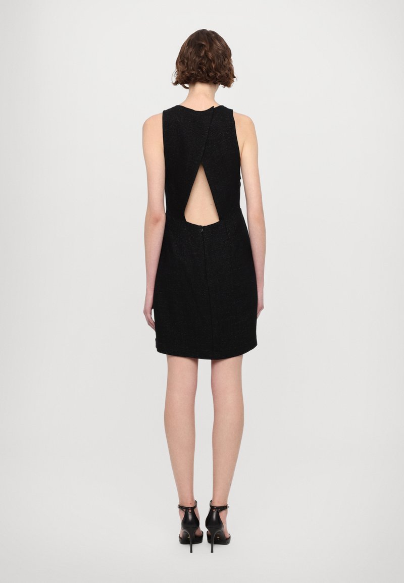 Czarna sukienka bez rękawów z wycięciem na plecach i zapięciem na zamek. Tkanina ma teksturowane wykończenie. Noszona z czarnymi sandałami na obcasie.