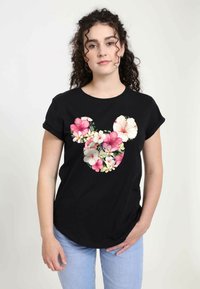 Sort t-shirt med korte ærmer med et blomsterdesign af Mickey Mouse i pink og hvide blomster, sat mod en ensfarvet baggrund.