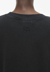 Camiseta de algodón negra con cuello redondo y un logo sutil en relieve en la parte trasera. Textura suave con un ajuste relajado.