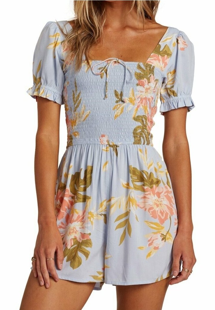 Donna che indossa unanzuolo floreale blu chiaro con maniche corte a sbuffo, corpetto smock, scollatura quadrata e dettaglio con fiocco al centro del petto.