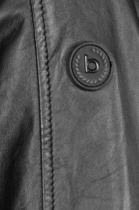Giacca di pelle nera con cuciture dettagliate e un distintivo circolare nero con la lettera bianca "b" circondata da un design di alloro.