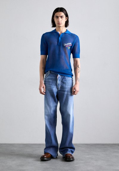 Blaues Strick-Polohemd mit Kragen, kurzen Ärmeln und gestickten Details, kombiniert mit hellblauen Schlagjeans und braunen Schuhen.