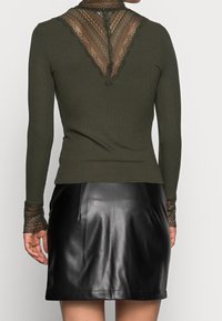 Olivgrön ribbad långärmad topp med spetsdetaljer bak och vid ärmsluten, matchad med en svart läder minikjol.