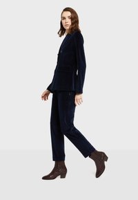 Námornícky zamatový oblek s priliehavým sakom a rovným strihom nohavíc, doplnený hnedými štruktúrovanými členkovými topánkami. Čistý dizajn a prispôsobený strih.