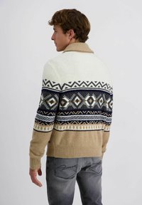 Gebreide trui met een crème bovenstuk, geometrische blauwe en tan patronen, en een beige geribbelde zoom. Heeft een sjaalkraag.