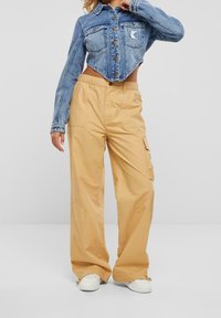 Chaqueta de mezclilla cortada en azul claro con botones metálicos y un parche bordado, combinada con pantalones cargo sueltos en beige con bolsillos laterales.