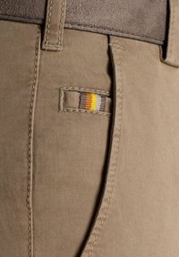 Bruine katoenmix broek met een zichtbare geweven label die gele, bruine en oranje strepen langs de zijnaad heeft. Gelaagd stofdetail.