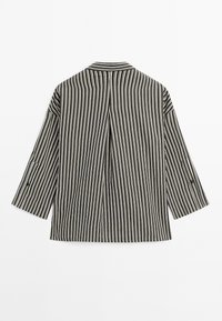 Veste à manches longues à rayures verticales noires et blanches, avec un pli central au dos et des détails de boutons sur les manches.