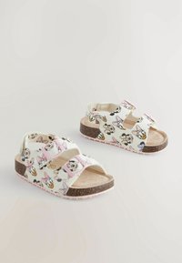 Kindersandalen met een witte synthetische bovenkant met prints van cartoonfiguren, roze verstelbare banden en een kurk-textuur voetbed.