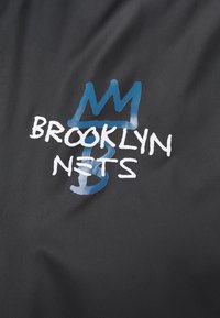 Tissu noir avec texte blanc "BROOKLYN NETS" superposé sur un graphique bleu de couronne et de symbole dollar.