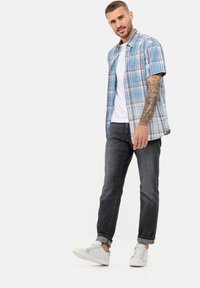Kurzärmliges kariertes Hemd in Blau, Weiß und Rot; über einem weißen T-Shirt getragen. Kombiniert mit dunkler Jeans und hellen Sneakers.