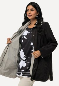 Svart, lätt, vattentät jacka med grå insida. Har dragkedjestängning, sidofickor och en avslappnad passform. Styla över en blommig blus.