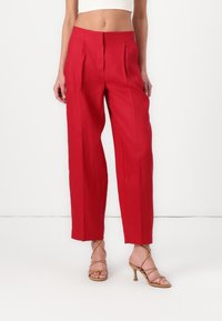 Pantalons rouges taille haute avec plis, design à jambe large, fabriqués en tissu léger. Associés à des sandales à talons hauts beige à lanières.
