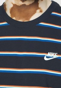 Mörkblå t-shirt med kort ärm och horisontella ränder i orange, ljusblått och vitt. Har en vit broderad Nike-logotyp på bröstet.