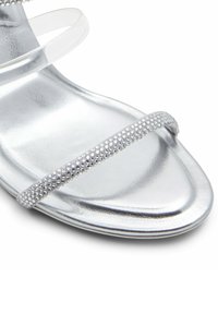 Stříbrné sandály na podpatku s metalickým povrchem, průhlednými pásky a rhinestonovými detaily na pásku. Elegantní design s otevřenou špičkou.