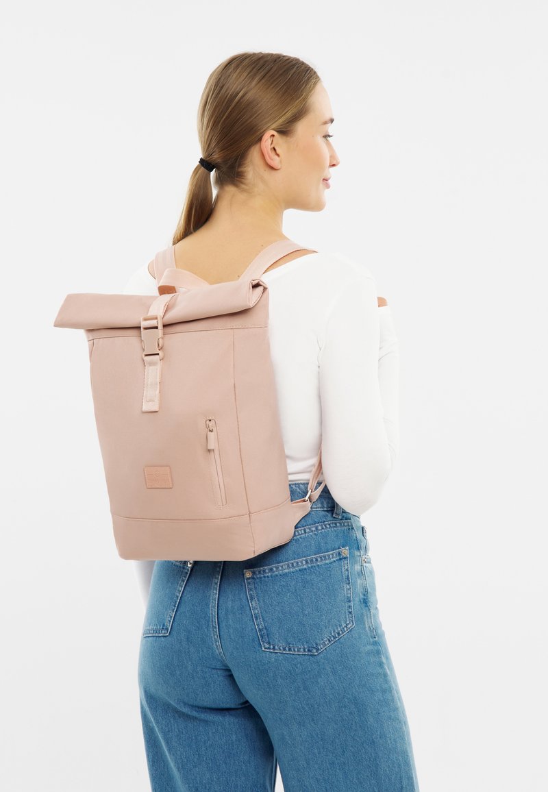 Zaino roll-top in morbido tessuto rosa, dotato di spallacci regolabili, una tasca frontale con zip e accessori laterali per una chiusura sicura.