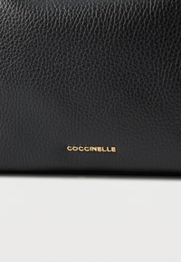 Sort tekstureret læderpung med et guld "Coccinelle"-logo på fronten, rektangulær form og glat, mat finish.