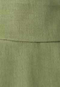 Grüner Stoff mit einer glatten Textur, der in der Mitte eine horizontale Naht aufweist. Das Material wirkt leicht und fein gewebt.