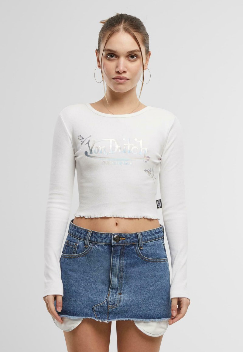 Vit långärmad croppad skjorta med metallisk "Von Dutch"-logotyp, kombinerad med en blå denim mini-skjorta med fransade kanter och fickor.