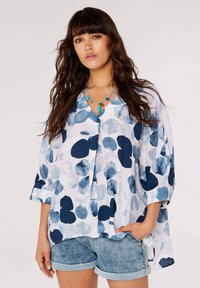 Chemise légère, bleue et blanche avec un col en V, ornée d'un motif abstrait de pois, à manches mi-longues et à coupe décontractée. Associée à un short en denim.
