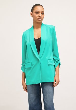 Turquoise blazer met een sjawl kraag, lange mouwen en twee voordoeken. Glad textuur en getailleerde pasvorm, gecombineerd met donkere jeans.