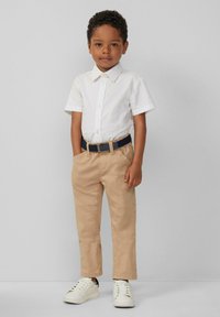 Witte kortemouwige button-up shirt, kaki broek met zakken, marineblauwe riem en witte sneakers met zwarte accenten. Eenvoudig, schoon design.