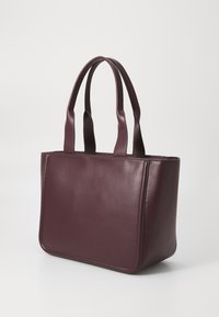 Sac fourre-tout en cuir bordeaux avec texture lisse, forme rectangulaire et deux poignées robustes. Présente un design minimaliste sans accessoires visibles.
